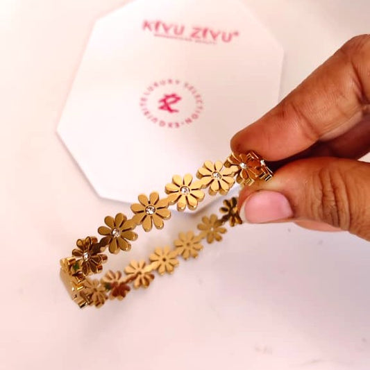 Detailed gold-tone flower charm bracelet on a delicate chain, feminine botanical jewelry style.